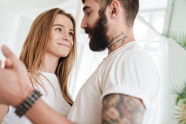 Romantik bir çiftin evdeki parlak odada sarılıp dans etmesi.