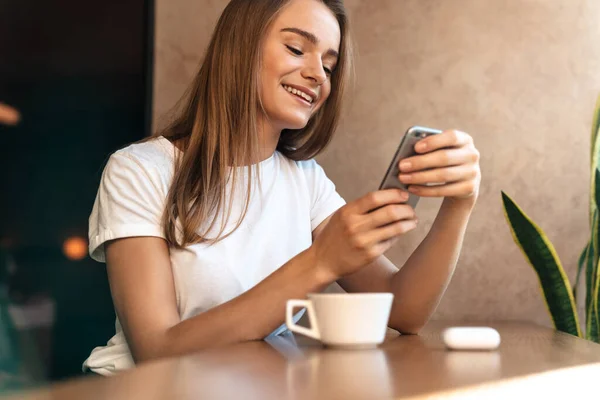 Photo Smiling Young Woman Drinking Coffee Using Cellphone While Sitting — Stock Photo, Image