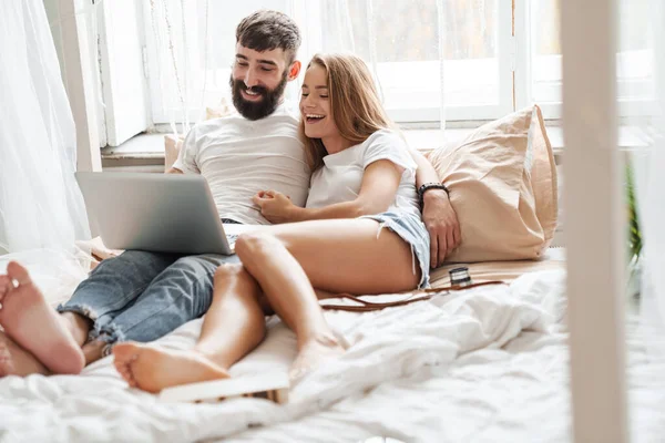 在家里明亮的房间里 一对浪漫快乐的情侣躺在床上 用笔记本电脑拥抱的情景 — 图库照片