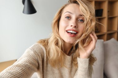 Evde gülümseyen neşeli genç bir kadının resmi. Bir selfie çek..