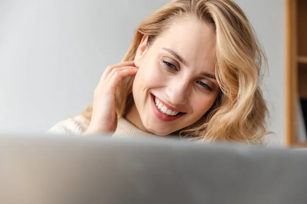 ラップトップコンピュータを使って屋内で家にいるかなり笑顔の楽観的な若い女性のイメージ — ストック写真