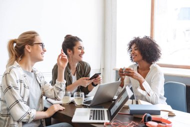 Bir grup çok ırklı ve neşeli genç kadın birlikte kahve içiyorlar.