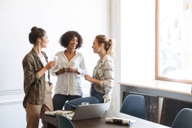 Bir grup çok ırklı ve neşeli genç kadın birlikte kahve içiyorlar.