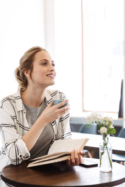 Härlig Ung Kvinna Läser Bok Medan Sitter Caféet Inomhus Dricka — Stockfoto