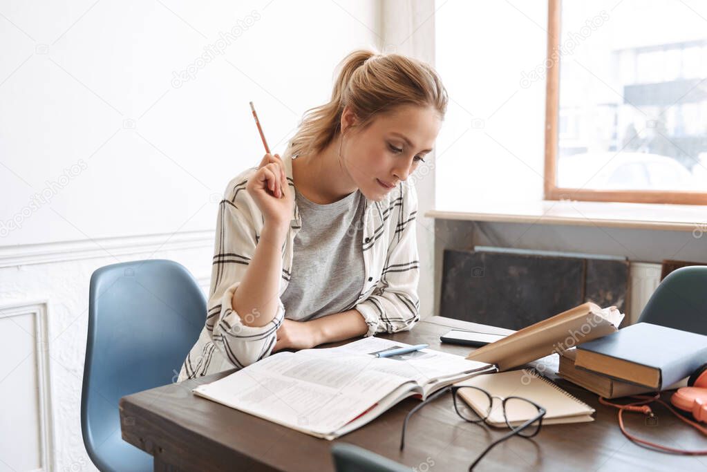 Attractive young girl student doing homework at the cafe indoors, reading books