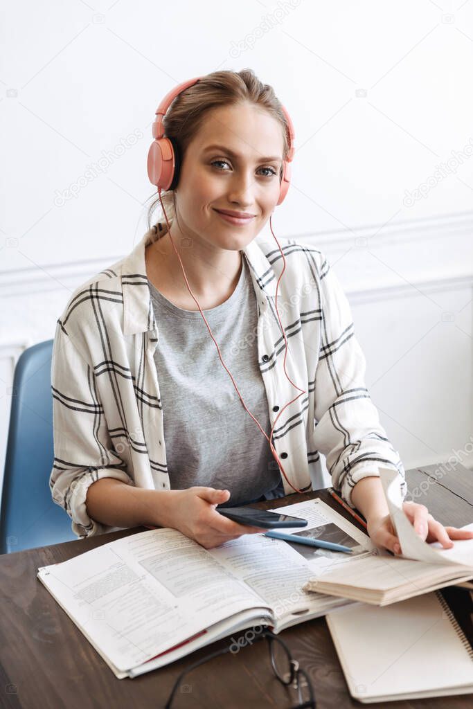 Attractive young girl student wearing headphones, doing homework at the cafe indoors, reading books