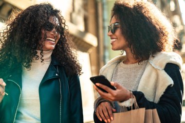 İki güzel, genç, şık Afrikalı kadın sokakta birlikte yürüyor, cep telefonu kullanıyor, konuşuyor.