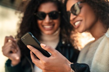 İki güzel, genç, şık Afrikalı kadın sokakta birlikte yürüyor, cep telefonu kullanıyor, konuşuyor.