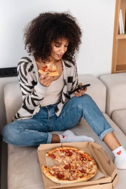 İyimser, pozitif, güzel, evde oturan Afrikalı bir kadının görüntüsü. Telefonda pizza yiyip sohbet ediyorlar..