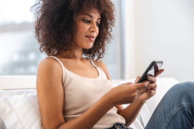 Evde cep telefonu kullanan konsantre olmuş Afrikalı bir kadının görüntüsü.