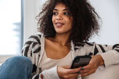 Evde cep telefonu kullanan gülümseyen Afrikalı genç bir kadın..