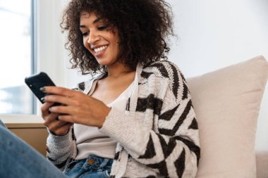 Neşeli, mutlu, iyimser, evde cep telefonu kullanan Afrikalı bir kadının görüntüsü..