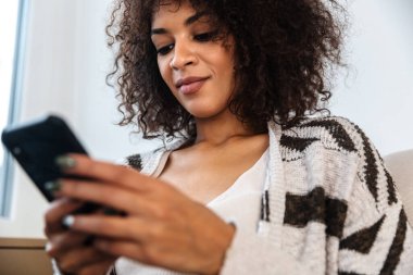 Evde cep telefonu kullanan pozitif iyimser Afrikalı bir kadının görüntüsü.