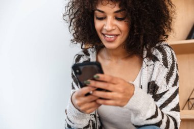 Neşeli, mutlu, iyimser, evde cep telefonu kullanan Afrikalı bir kadının görüntüsü..