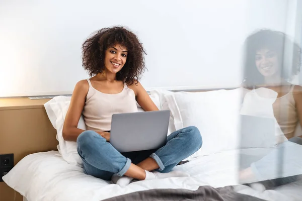 图片中快乐快乐的年轻非洲妇女在家里用手提电脑坐在床上 — 图库照片
