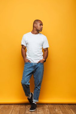 Sarı arka planda duran çekici, kendinden emin genç bir adamın tam boy portresi.