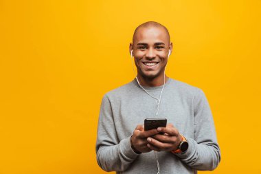 Sarı arka planda durup kulaklıkla müzik dinleyen, elinde cep telefonu tutan çekici, kendine güveni tam bir Afrikalı genç adamın portresi.