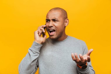 Elinde cep telefonu olan, sarı arka planda dikilen çekici, sinirli, sıradan bir Afrikalı adamın portresi.