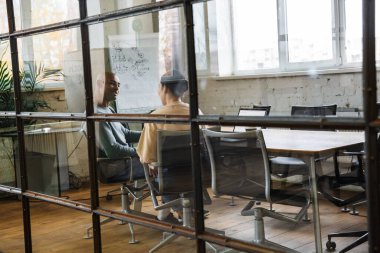 Çok ırklı genç kadın ve erkek iş arkadaşlarının masada oturup ofiste dizüstü bilgisayarlar üzerinde çalışması