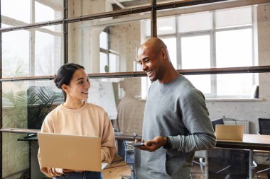 Ofiste dizüstü bilgisayarla çalışan gülümseyen genç bir meslektaşın görüntüsü.