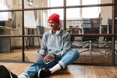 Pozitif iyimser bir Afrikalı gencin dizüstü bilgisayar ve cep telefonu kullanarak yerde oturması.