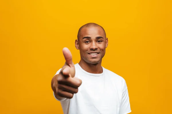 黄色の背景の上に立っている魅力的な笑顔の自信に満ちたカジュアルな若いアフリカの男の肖像 カメラで指を指す — ストック写真