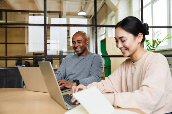 多民族の若い女性と男性の同僚がテーブルに座ってオフィスのノートパソコンで作業するイメージ — ストック写真