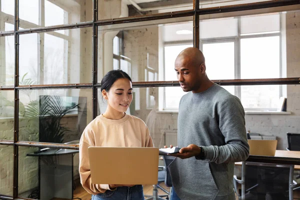 Image of a young concentrated multiracial colleagues indoors work in office with laptop computer.