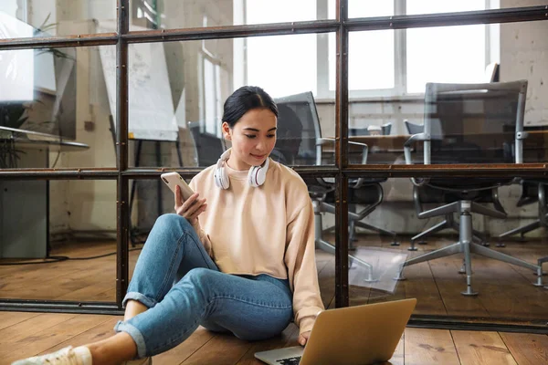 正のアジアの若い女性のイメージは ラップトップコンピュータと携帯電話を使用して床の上に屋内に座っている — ストック写真