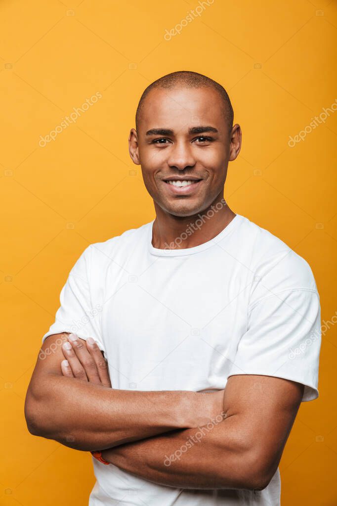 Portrait of an attractive smiling confident casual young african man standing over yellow background