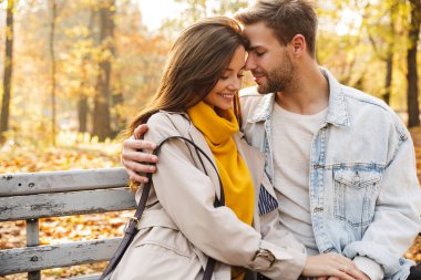 Güz parkında yürürken bankta oturan çekici beyaz bir çift.