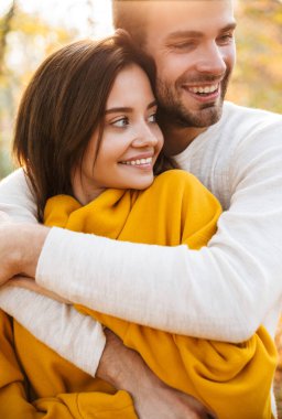 Güz parkında yürürken birbirine aşık genç beyaz bir çiftin görüntüsü.