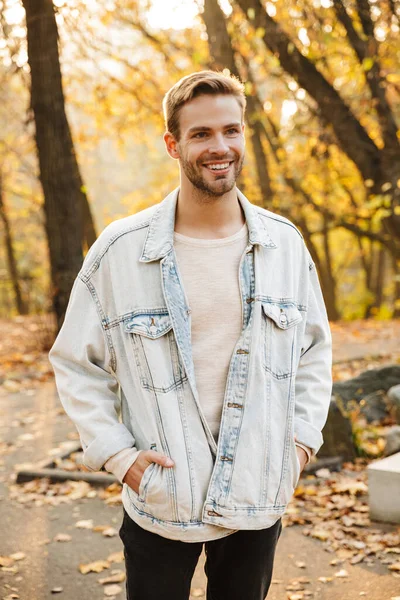 公園を歩いている間に笑顔デニムジャケットでハンサムな若い白人男性のイメージ — ストック写真
