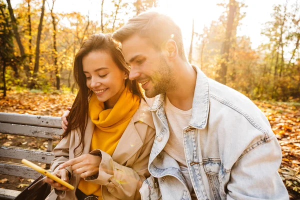 Allegro Giovane Coppia Seduta Una Panchina Nel Parco Autunnale Utilizzando — Foto Stock