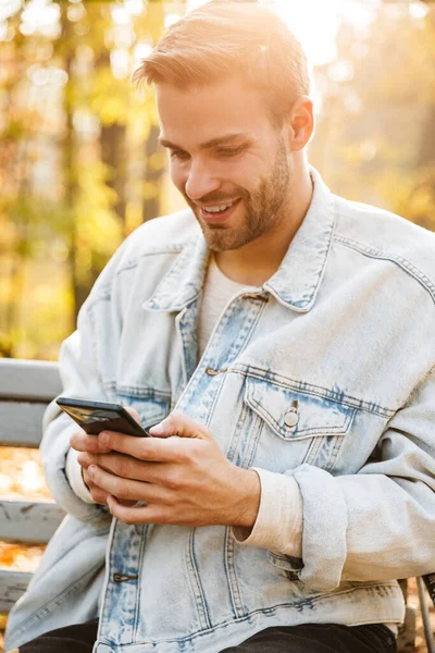 Handsome Smiling Young Man Sitting Bench Autumn Park Using Mobile — Stock Photo, Image