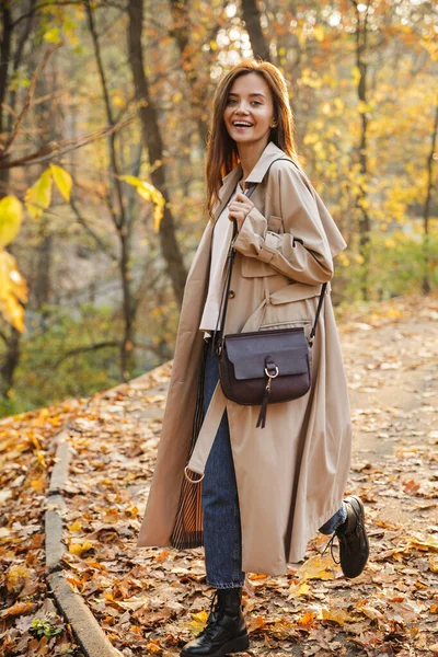 코트를 머리의 여성이 웃으며 공원에서 산책하는 — 스톡 사진