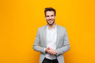 Sarı arka planda tek başına duran yakışıklı, gülümseyen genç iş adamı kameraya bakıyor.