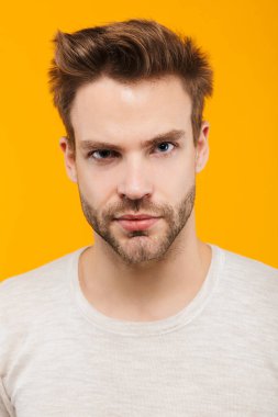 Sarı arka planda duran pulslu giyen çekici bir delikanlının kameraya baktığı yakın plan.