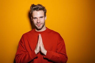 Çekici gülümseyen genç adam sarı arka planda tek başına duruyor.