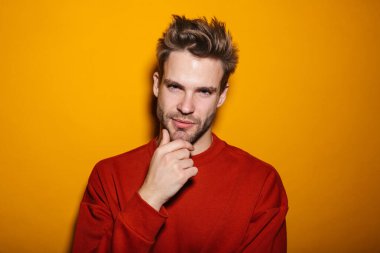 Çekici, düşünceli, gülümseyen, pulslu giyinen genç adam sarı arka planda tek başına duruyor.