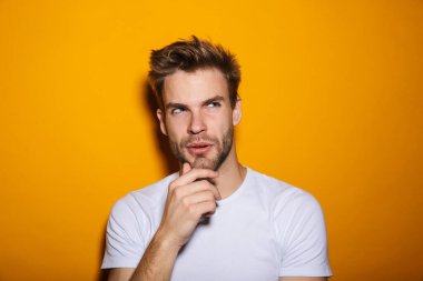 Çekici düşünceli genç adam sarı arka planda tek başına duruyor, başka tarafa bakıyor.