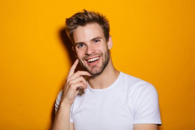 Çekici, mutlu, düşünceli, pulslu giyen genç adam sarı arka planda izole bir şekilde kameraya bakıyor.