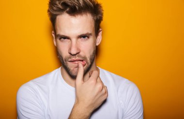 Yakışıklı, baştan çıkarıcı, sarı arka planda izole bir şekilde poz veren genç adam, kameraya bakıyor.