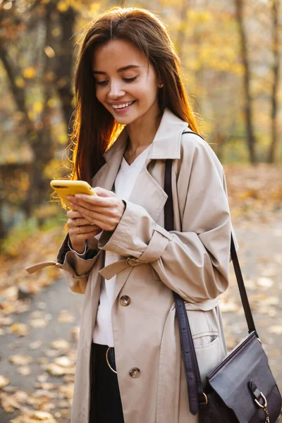 秋のコートで若いブルネットの女性の画像笑顔と秋の公園で屋外を歩く — ストック写真