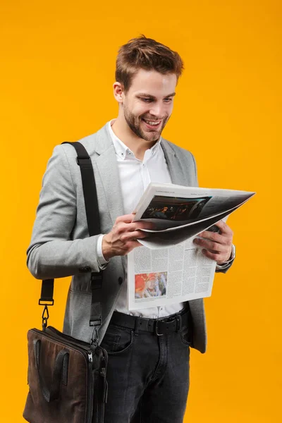 黄色の背景の上に隔離された立っているジャケットを身に着けているハンサムな笑顔の若いビジネスマン バッグを運ぶ 新聞を読む — ストック写真