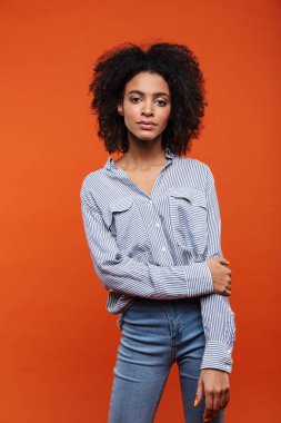 Gülümseyen çekici Afrikalı kadın günlük kıyafetler giyip kırmızı arka planda tek başına poz veriyor.