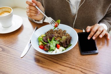 Kafede kulaklıkla ve cep telefonuyla müzik dinleyen Afrikalı Amerikalı genç bir kadının portresi.
