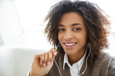 Parlak odada gülümseyen ve kulaklık kullanan güzel Afro-Amerikan kadının portresi.