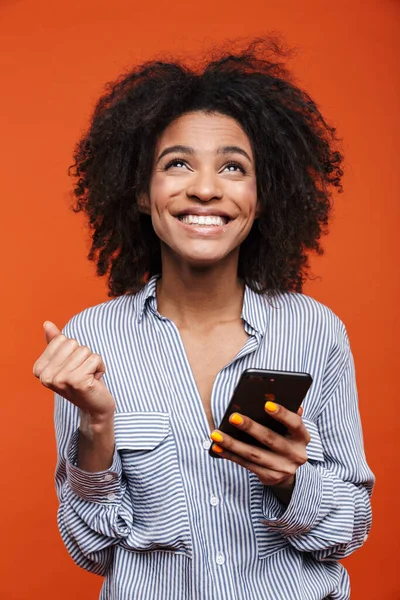 赤の背景に隔離された携帯電話を使用して魅力的な若いアフリカの女性を笑顔 — ストック写真