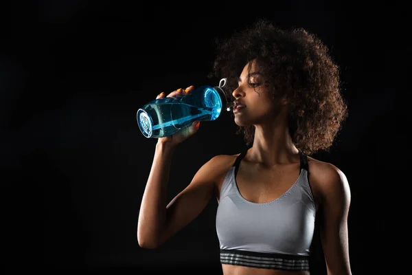 黒の背景に隔離された作業中に水を飲む美しいアフリカ系アメリカ人のスポーツ女性のイメージ — ストック写真
